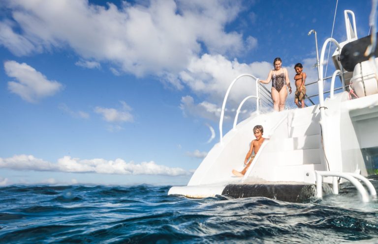 Three people on a boat's steps above the ocean on a sunny day.