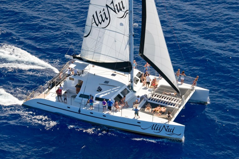 Catamaran sailing with people on deck in blue ocean.