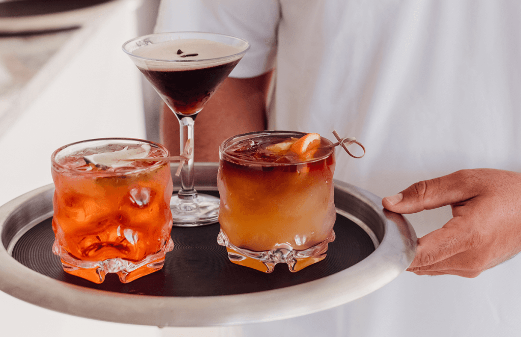 Person holding tray with three cocktails, including an espresso martini and two on the rocks.