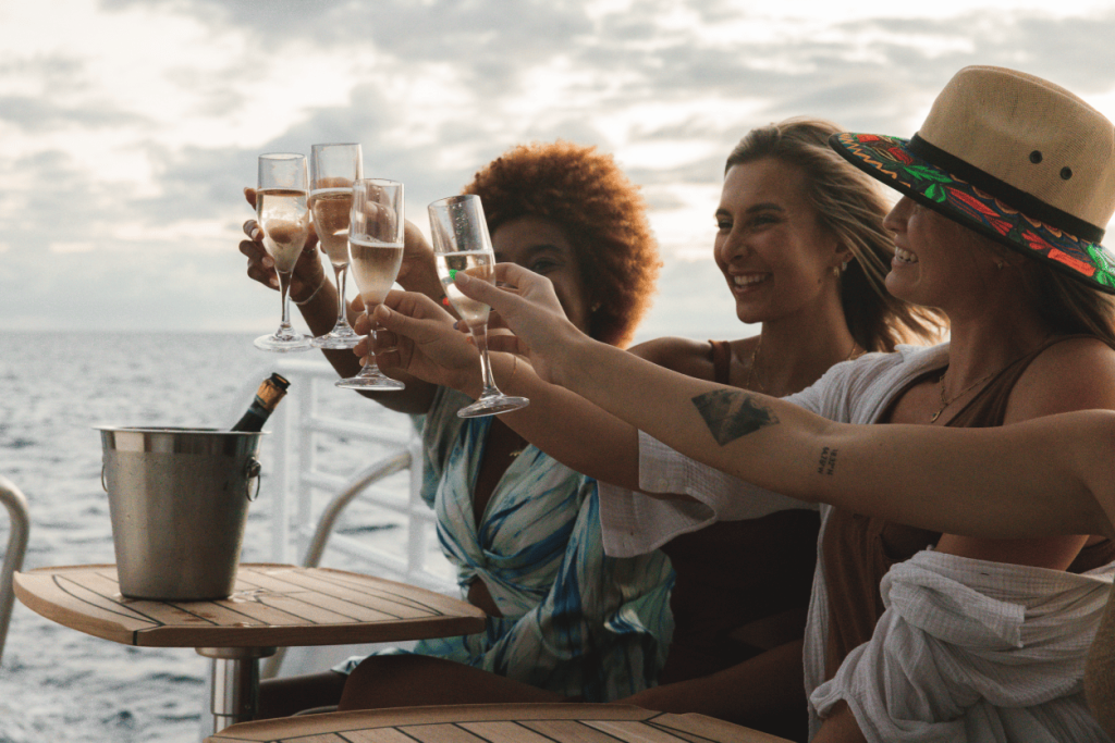 Four people toasting with champagne glasses on a boat at sunset.