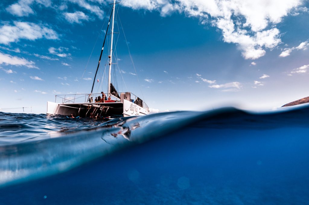 Partially submerged view of a sailboat on the ocean under a blue sky with clouds.