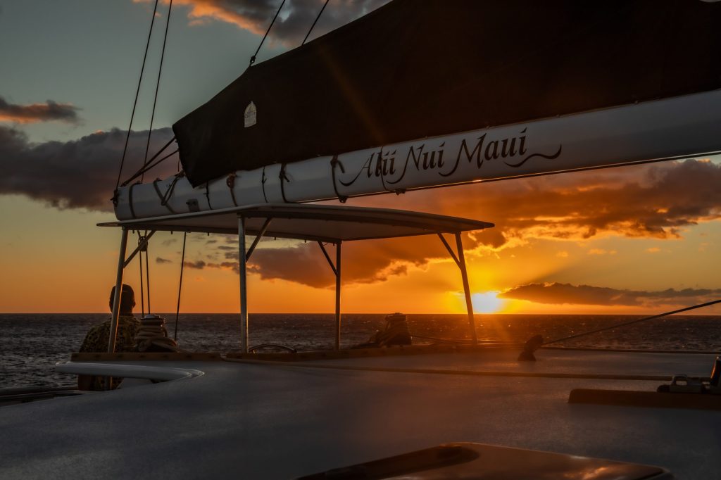 Sailboat at sea with sunset and clouds in the background.