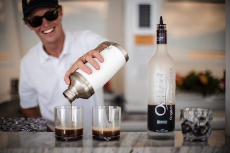 Person pouring drink into glasses beside a vodka bottle on a bar.