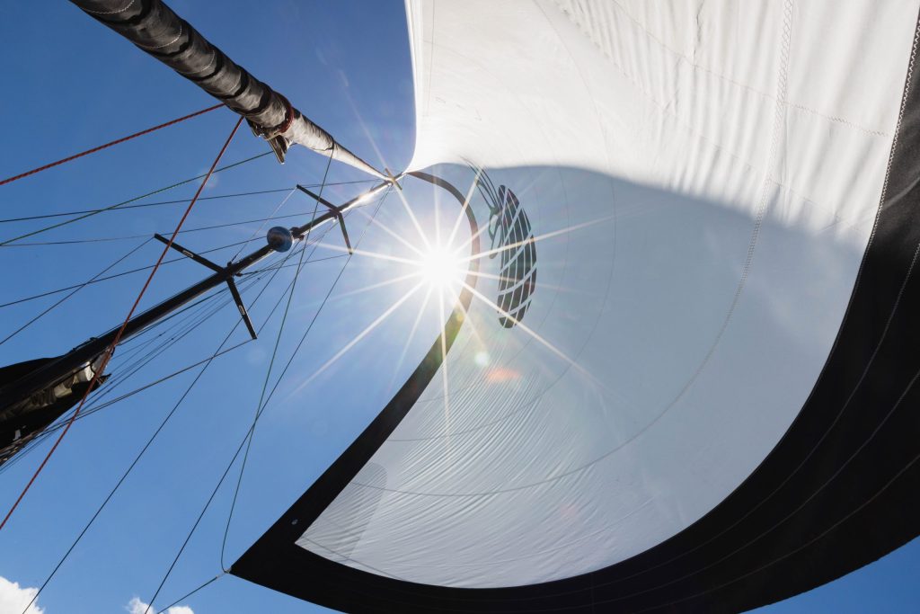 Looking up at a sail with sunlight shining through against a clear blue sky.