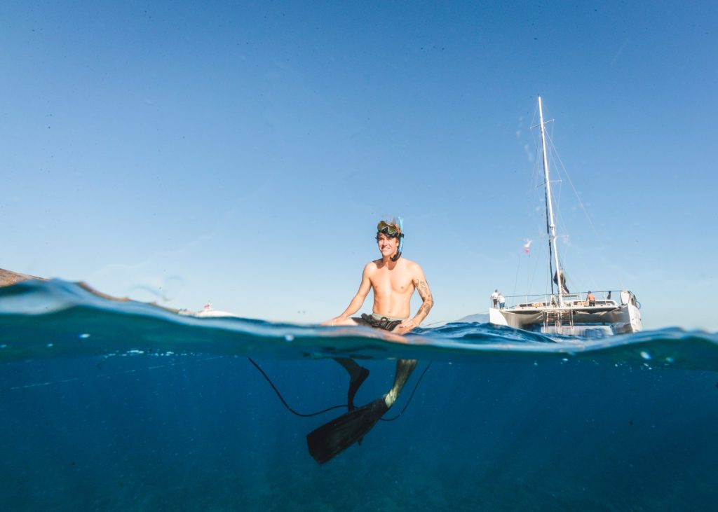Snorkeler in water near a sailboat on a clear day.