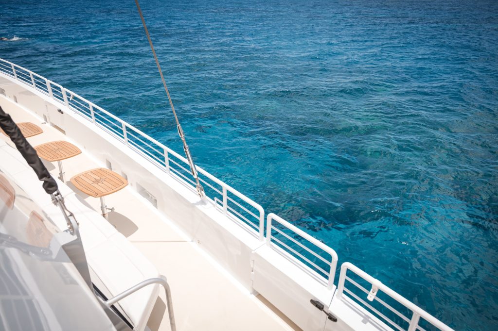 Deck of a boat with wooden stools overlooking clear blue ocean water.