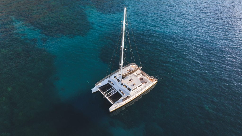 Aerial view of a catamaran sailing on clear blue ocean waters.