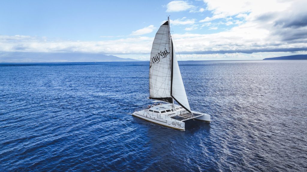 A sailboat navigating on a calm blue ocean under a partly cloudy sky.