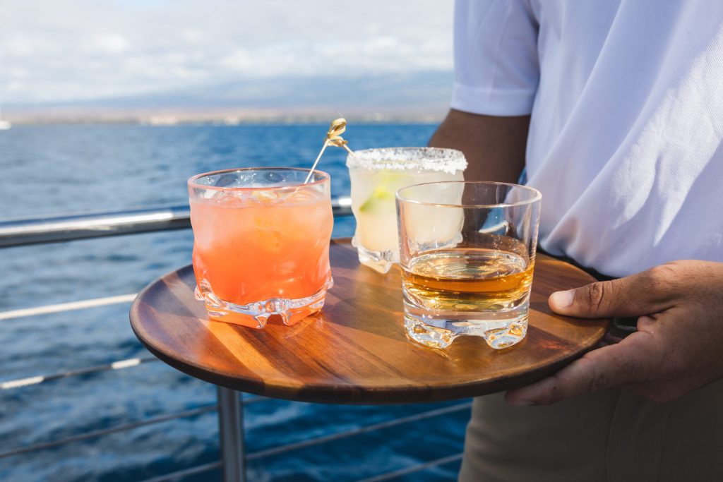 Person holding tray with three cocktails on a boat.