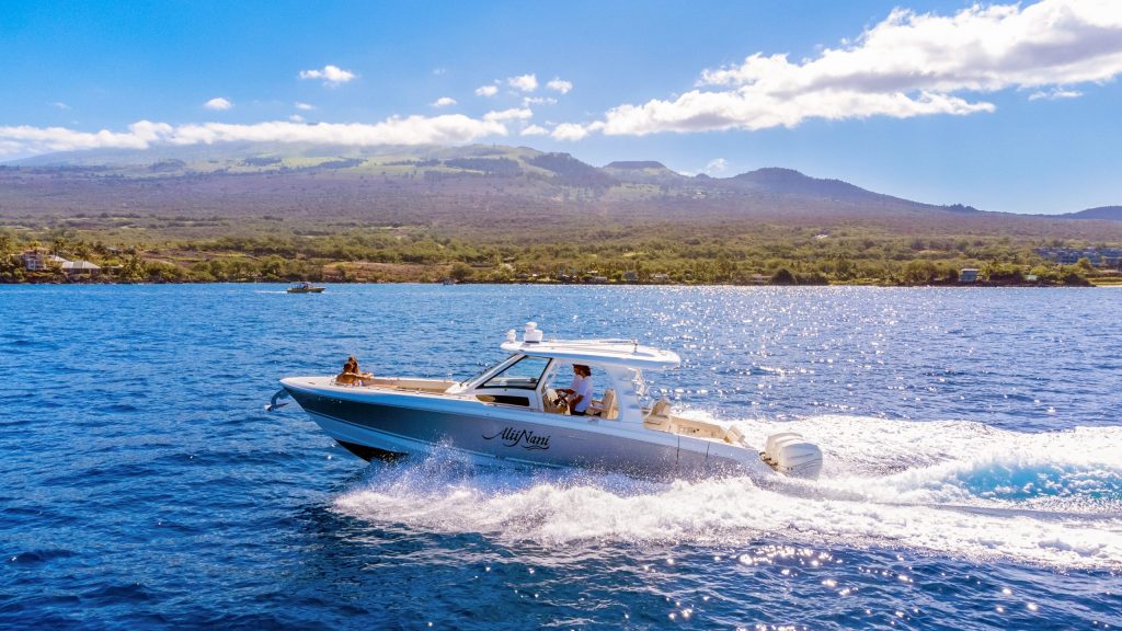 Motorboat speeding on blue water with mountains in the background.