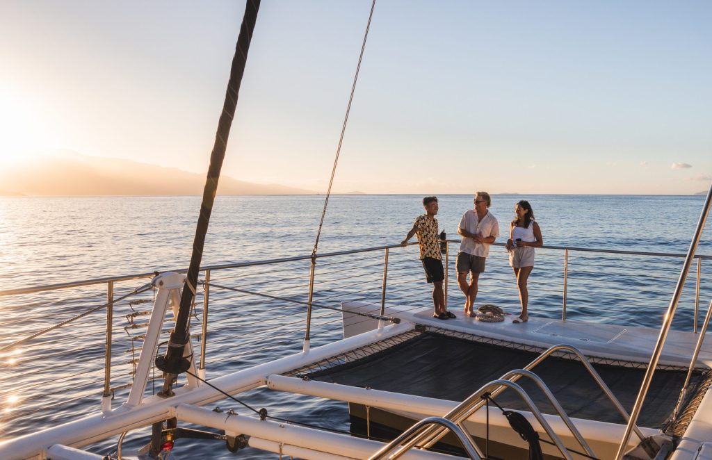 Three people relax on a yacht deck at sunset, overlooking the calm ocean.