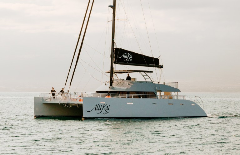Modern catamaran sailing on calm sea with two people on deck.