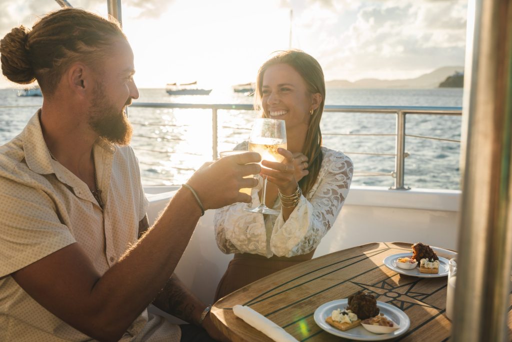 Couple on a boat toasting with drinks at sunset.