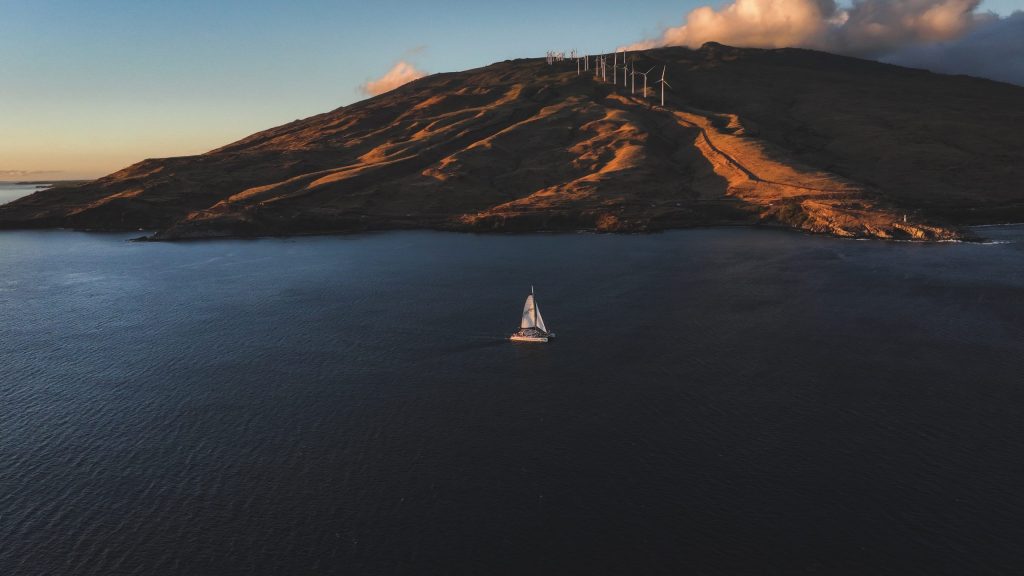 Sailboat on calm water near a hilly coastline with wind turbines.