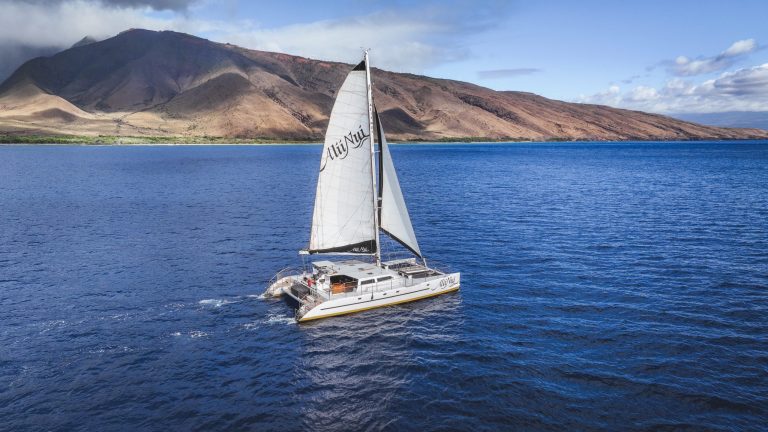 Sailboat on blue ocean with mountainous coastline in background.