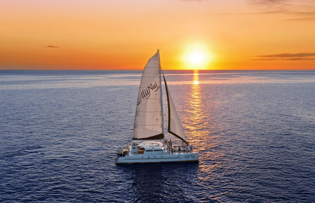 Sailboat on the ocean during sunset with orange and pink sky.