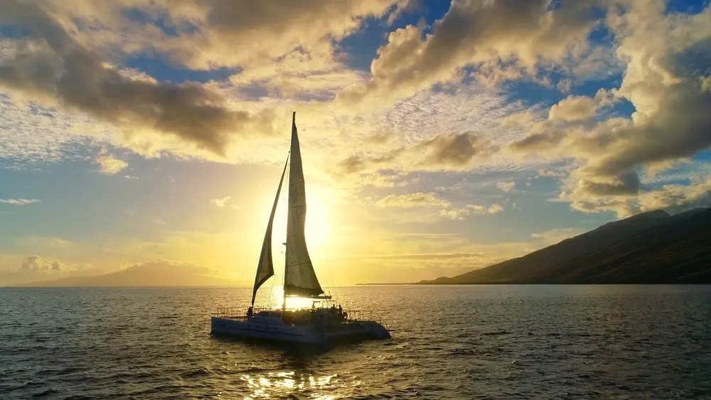 Sailboat on ocean silhouette against vibrant sunset with clouds.