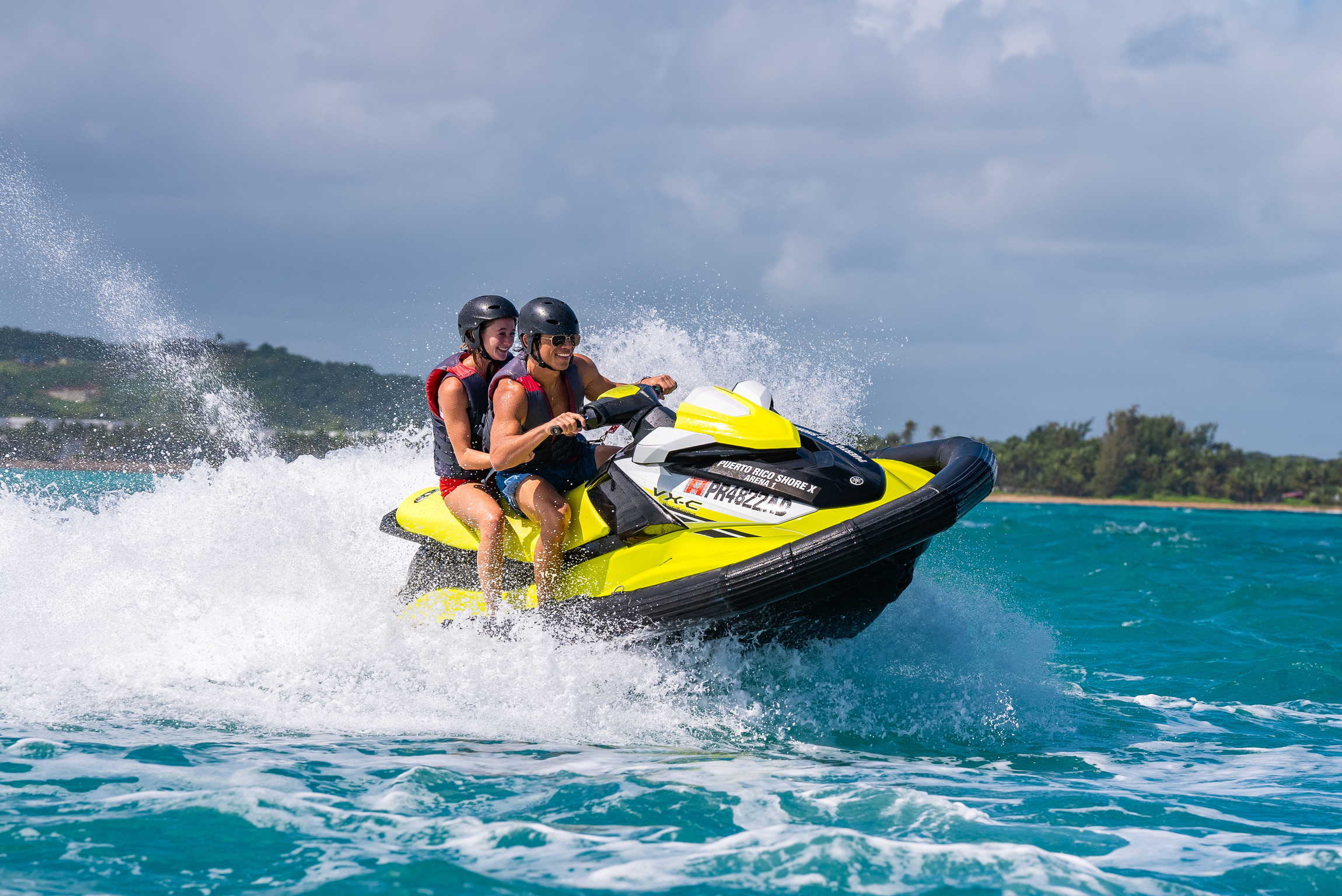 Two people on a yellow jet ski speeding over ocean waves.