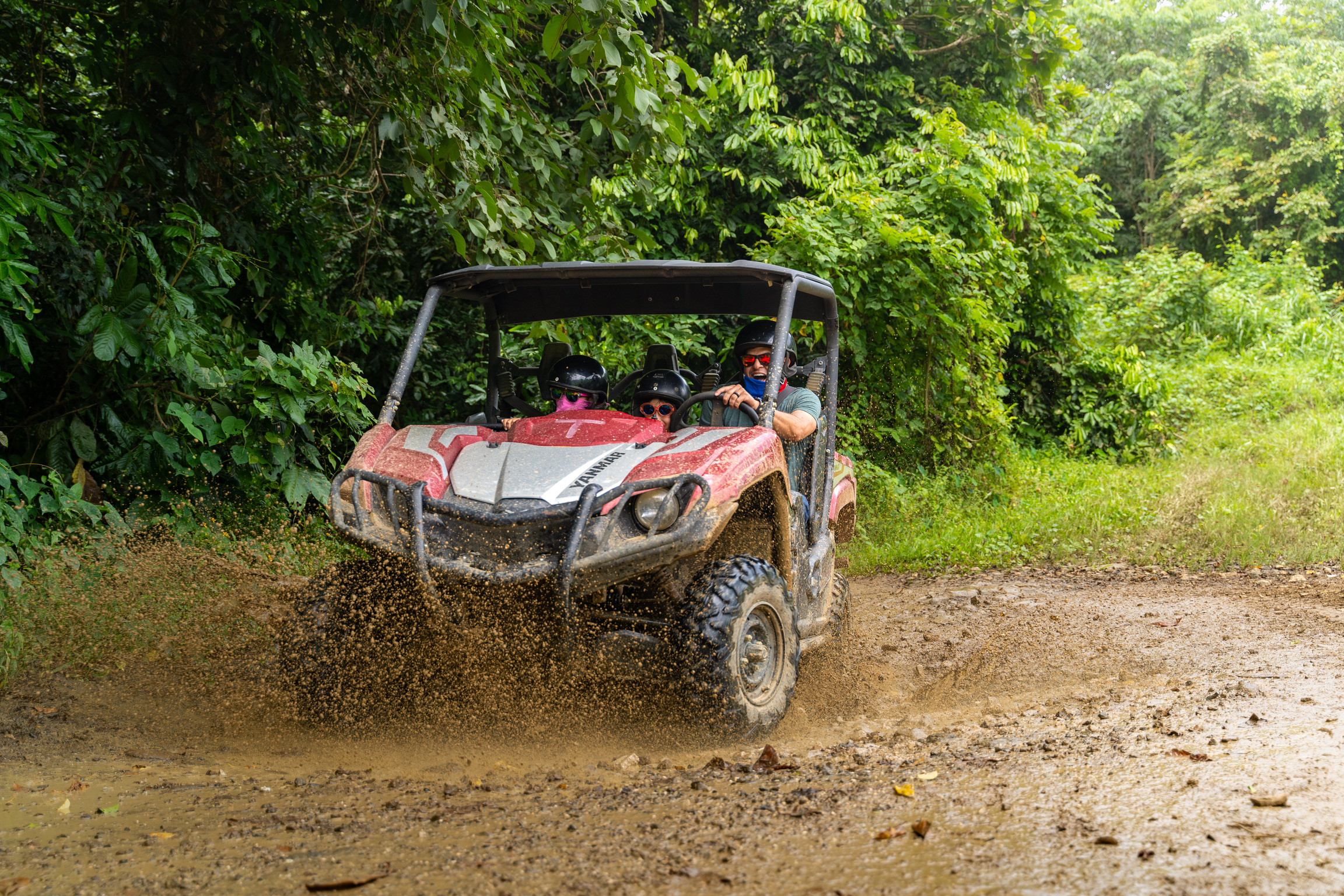 A red ATV splashing through a muddy trail in a forested area.