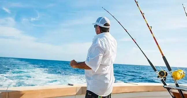 Man fishing on a boat in the ocean with fishing rods and blue sky.