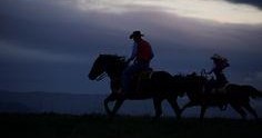 Silhouette of two horseback riders at dusk against a cloudy sky.