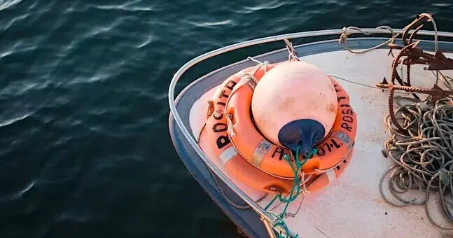Boat deck with lifebuoy and ropes beside blue water.