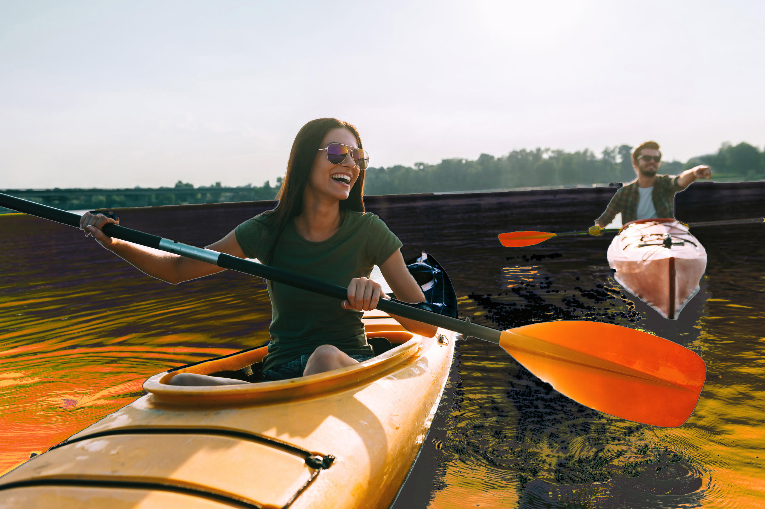 Two people kayaking on a calm lake with orange paddles.