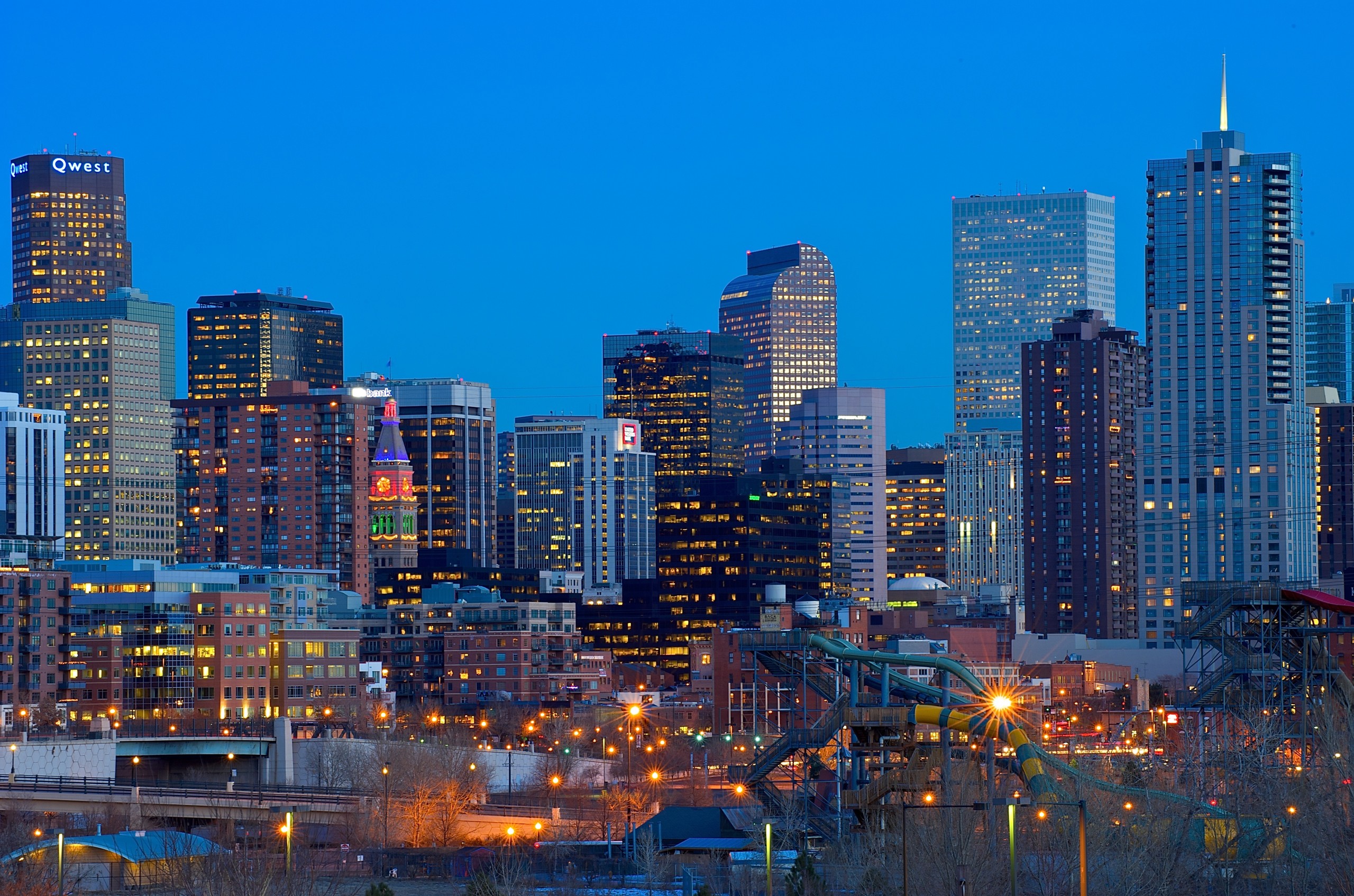Skyline of a city with tall buildings and bright lights at dusk.