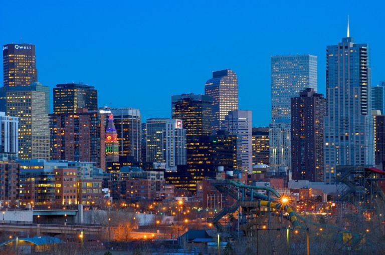 Skyline of a city with tall buildings and bright lights at dusk.