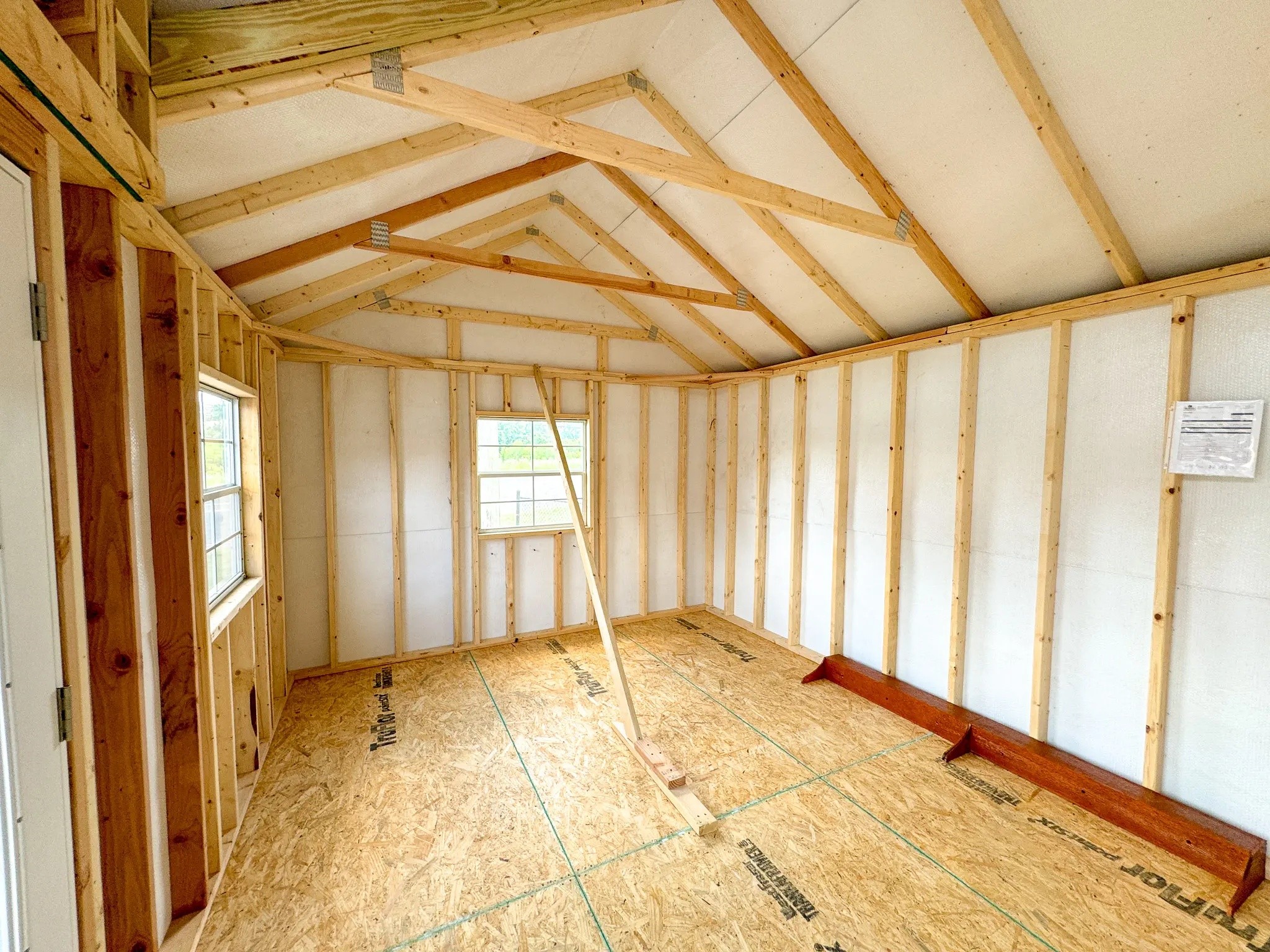 Interior of an unfinished wooden shed with exposed beams and two windows.