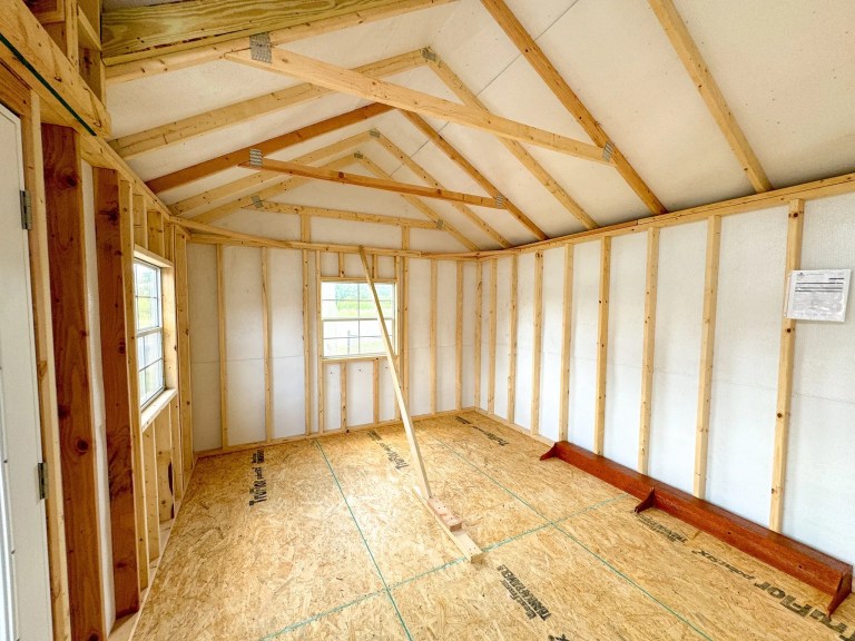 Interior of an unfinished wooden shed with exposed beams and two windows.