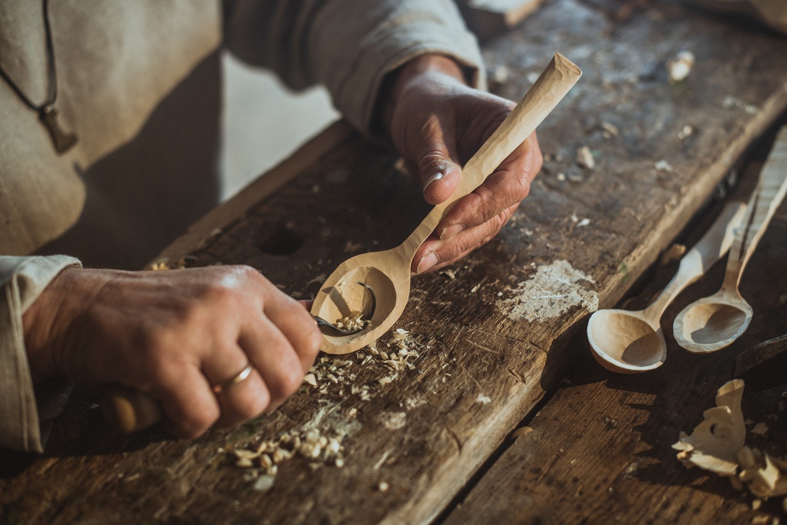Person carving wooden spoon at a rustic workbench.