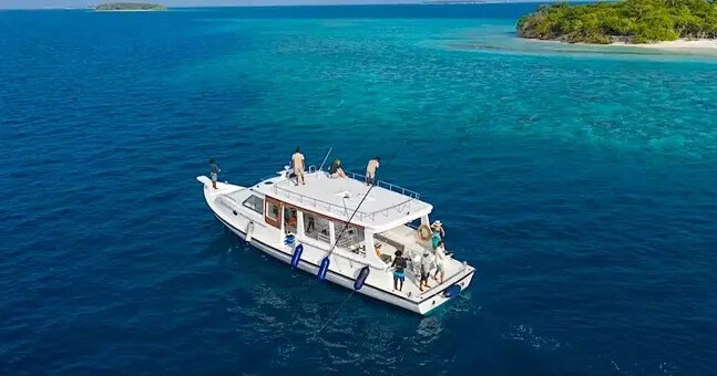 Boat with people in clear blue ocean near a small island.