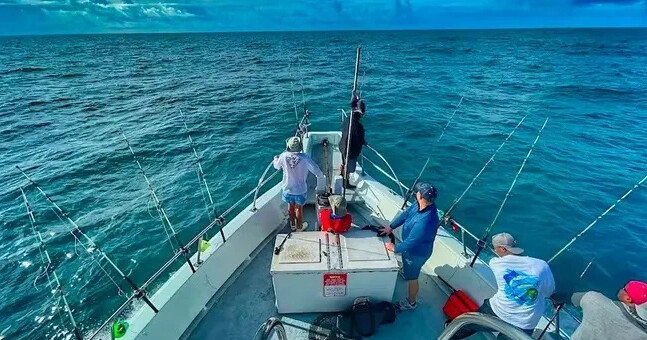 People fishing from a boat in the ocean under a blue sky.