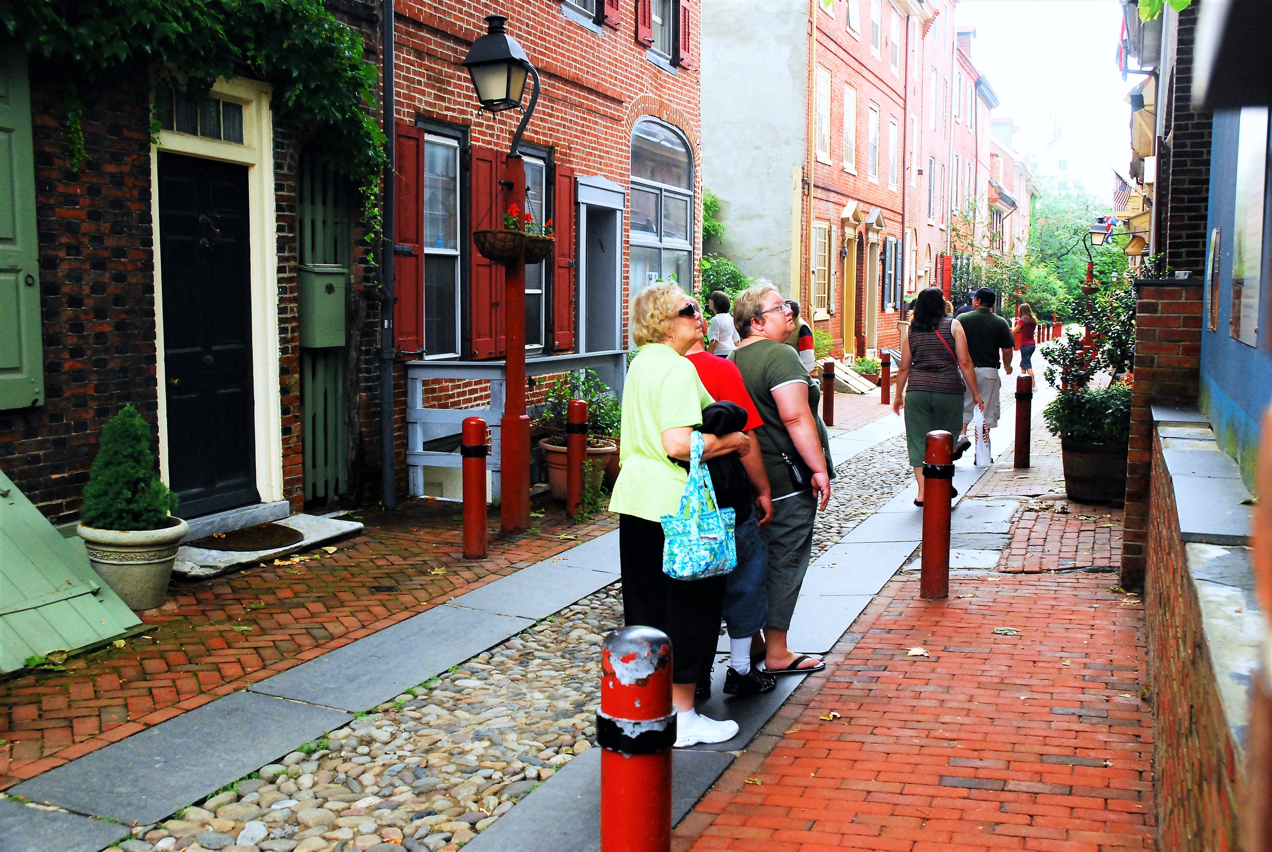 People walking on a narrow cobblestone street with brick buildings.