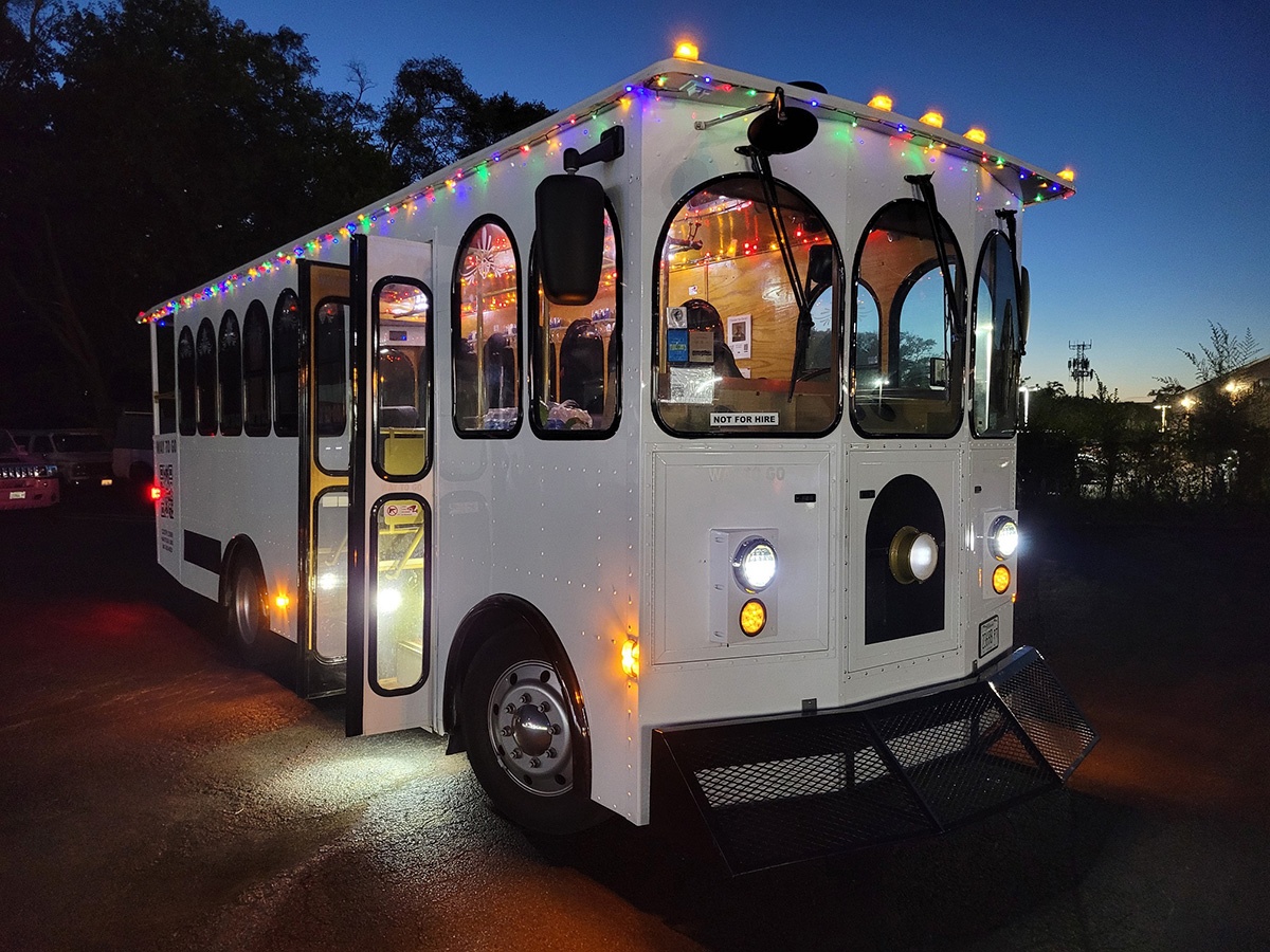 Illuminated white trolley bus with colorful lights at dusk.