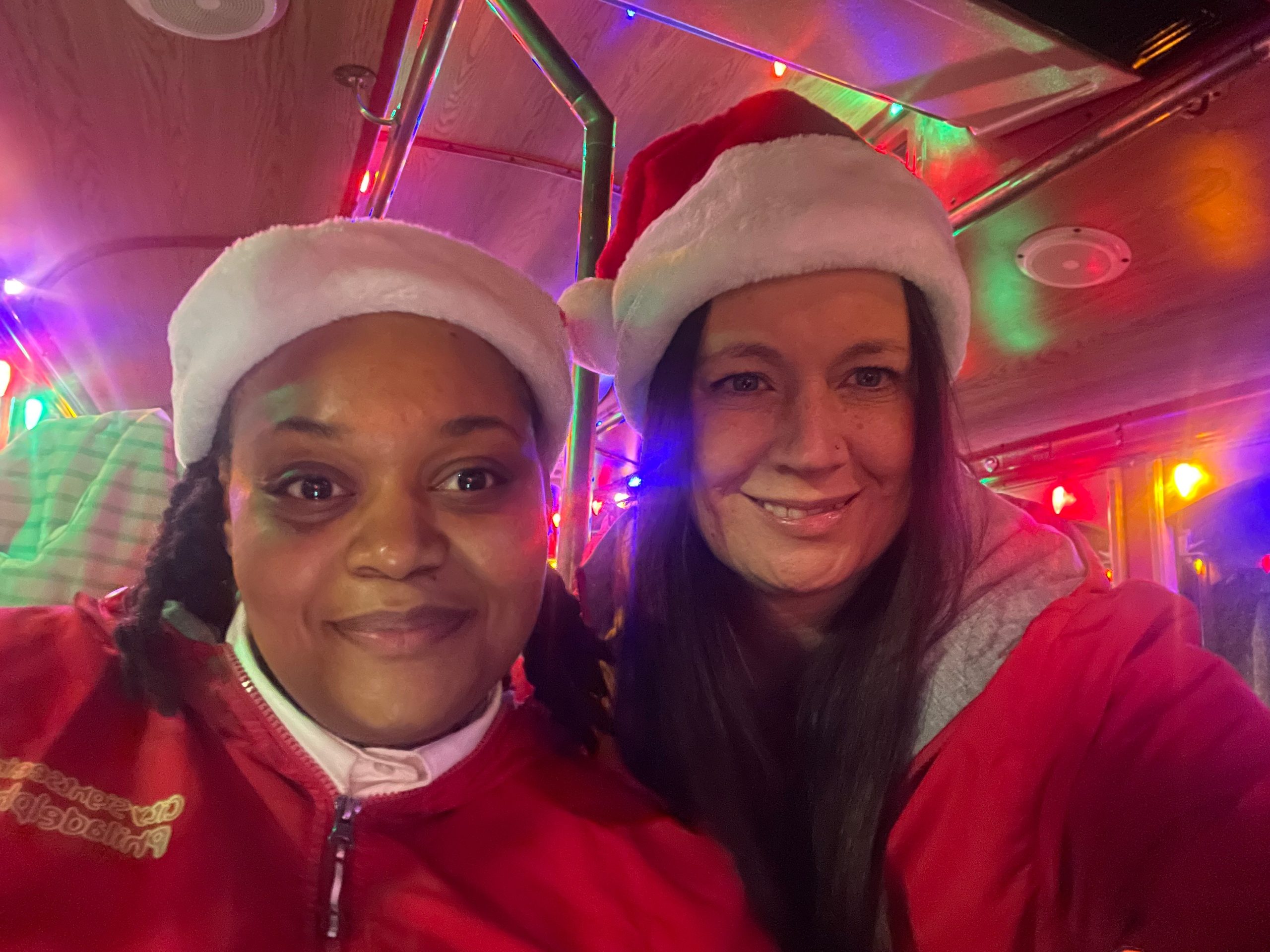 Two people wearing Santa hats, smiling indoors with festive lights.