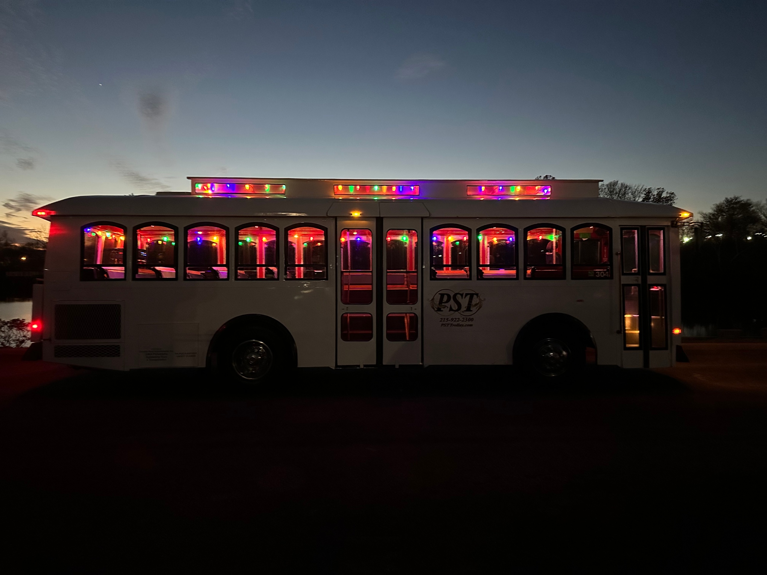 White trolley bus with colorful lights at dusk.