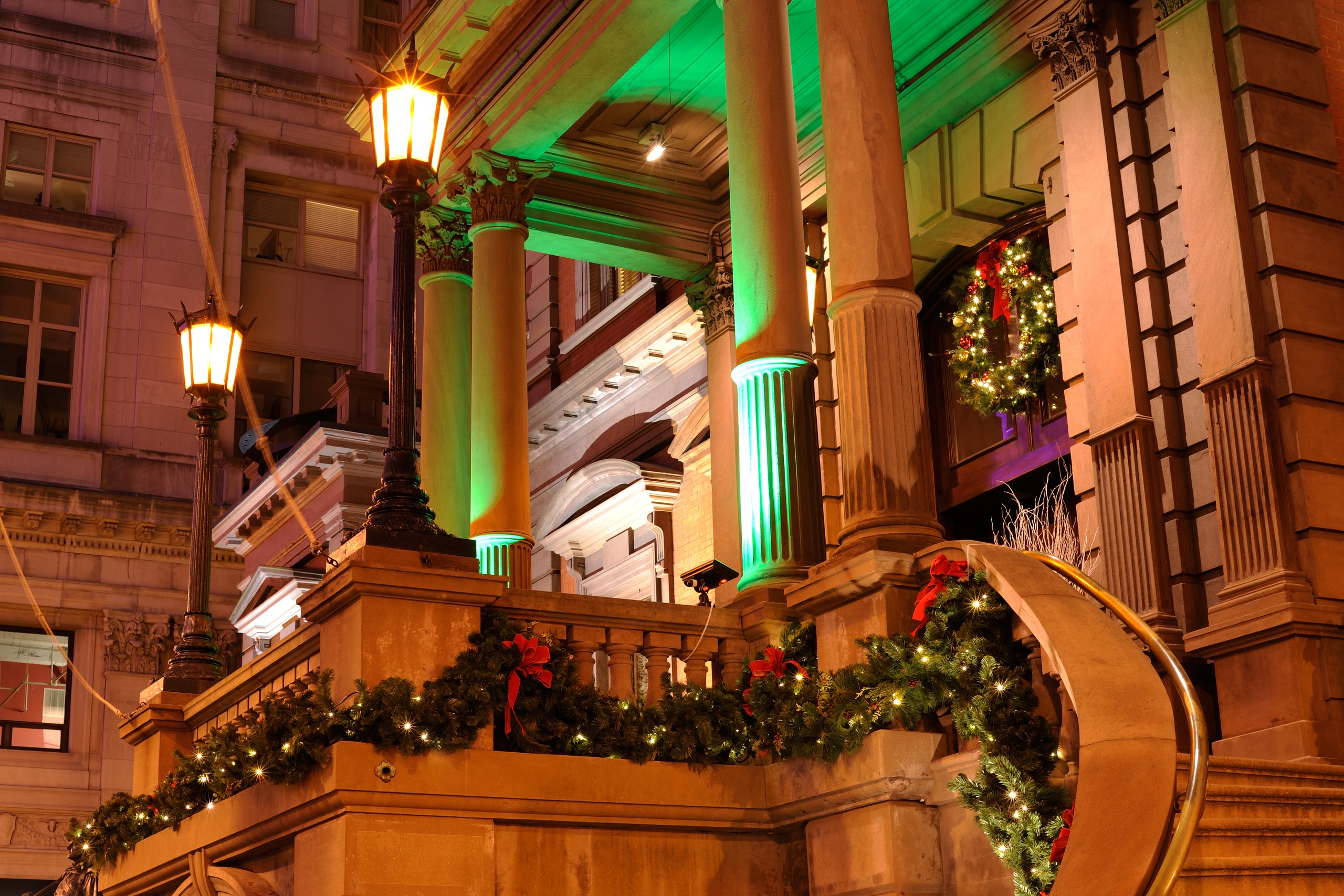 Festive building with columns, lit by green lights and adorned with holiday wreaths and garlands.