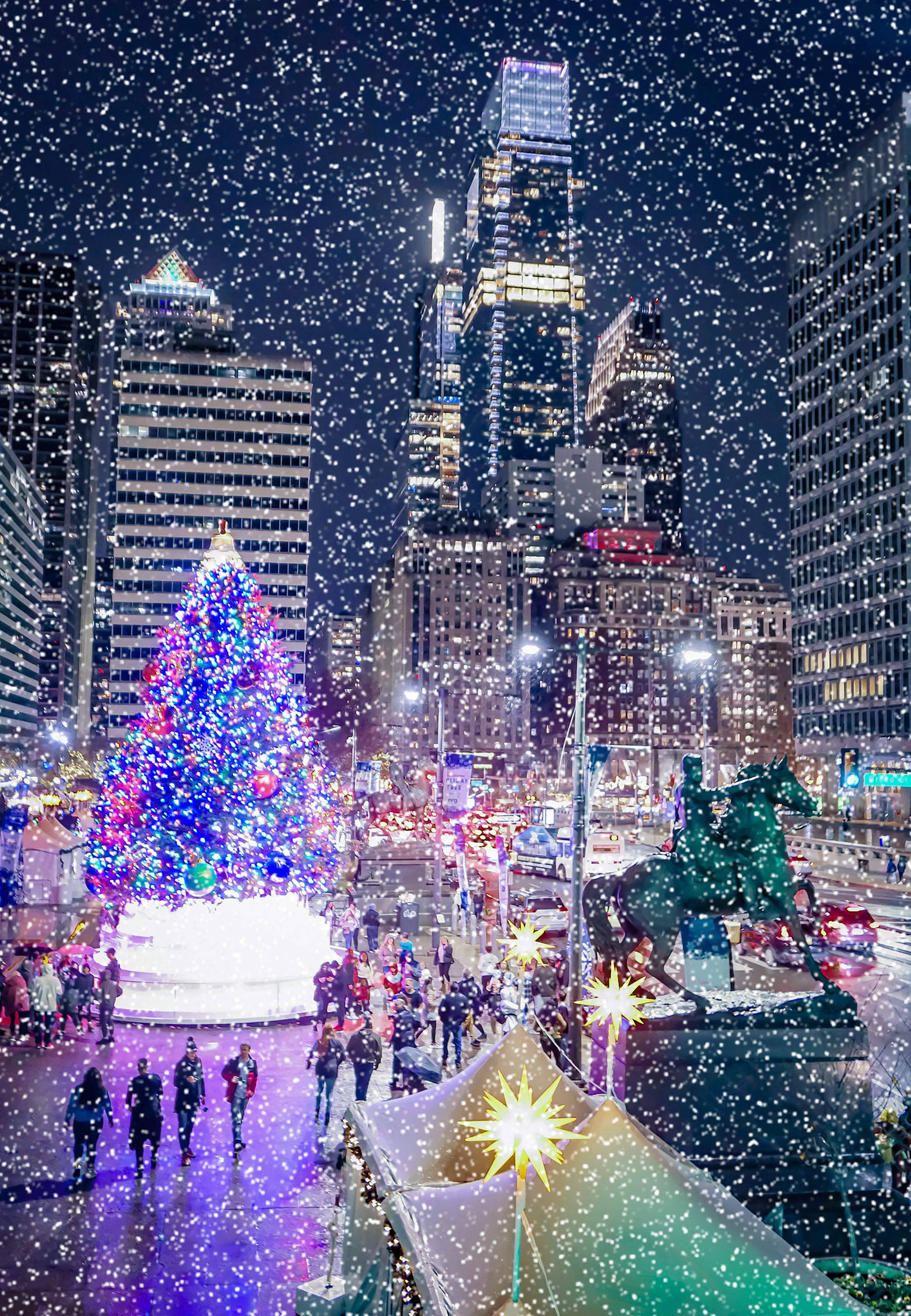 Snowy city scene with a large decorated Christmas tree and skyscrapers at night.