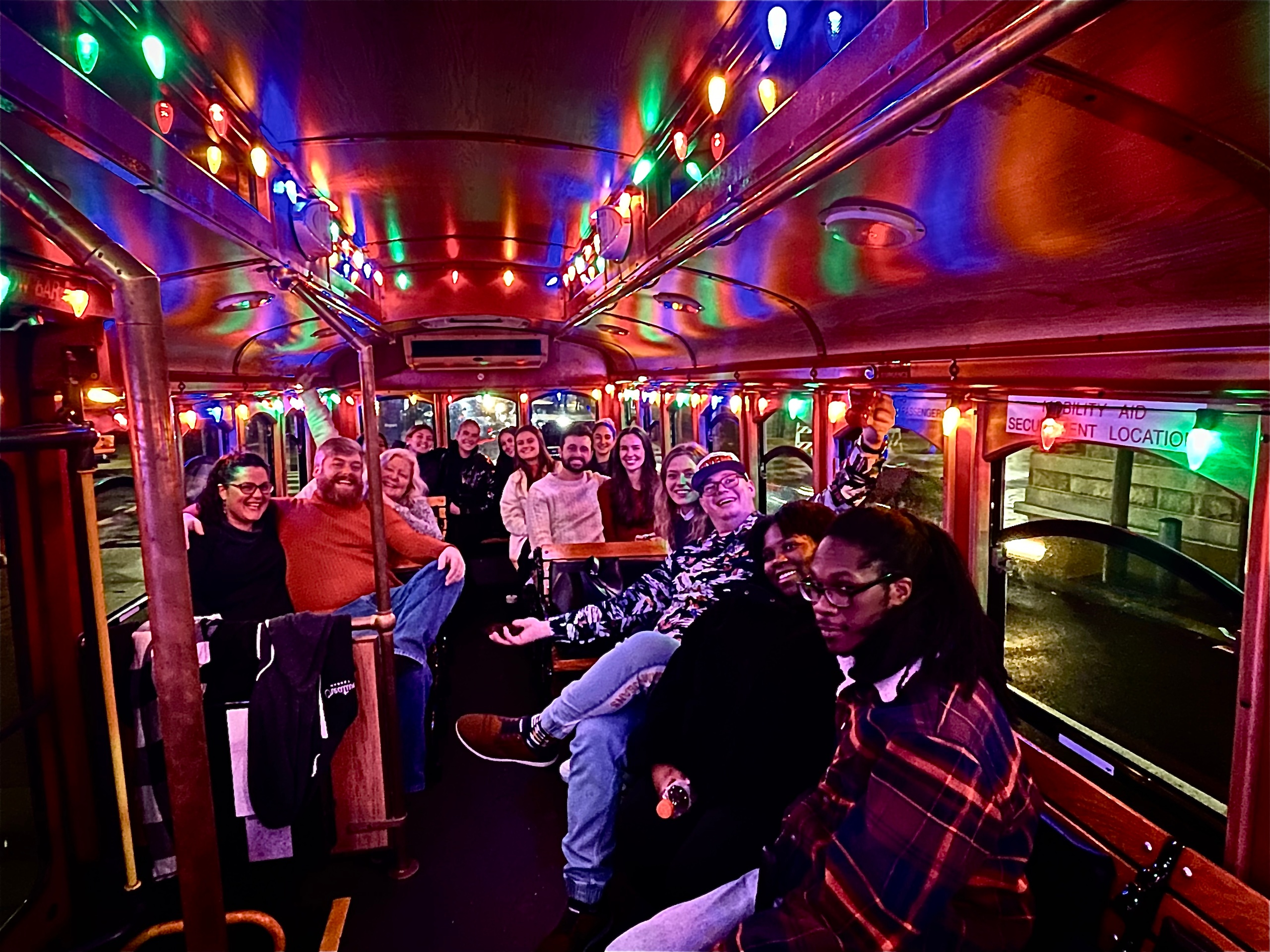 People smiling and sitting inside a festive, decorated bus with colorful lights.