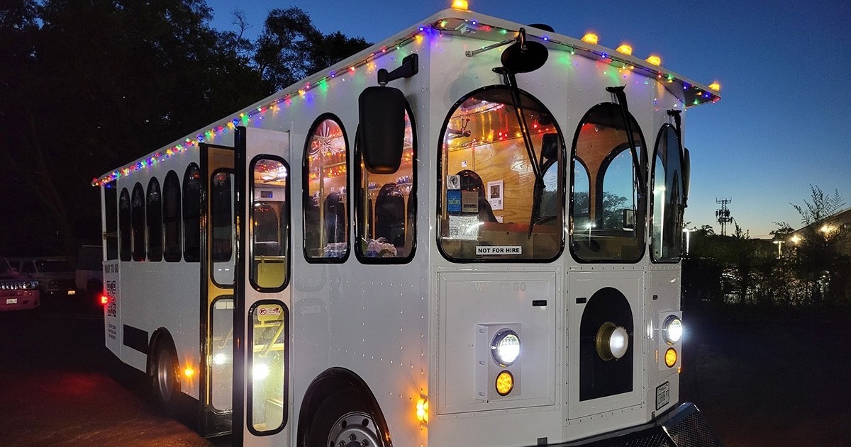 White trolley with colorful lights at dusk.