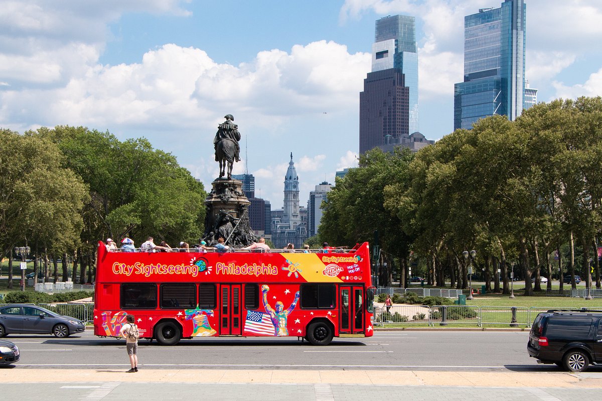 Tour bus with Philadelphia skyline and monument in background on a sunny day.