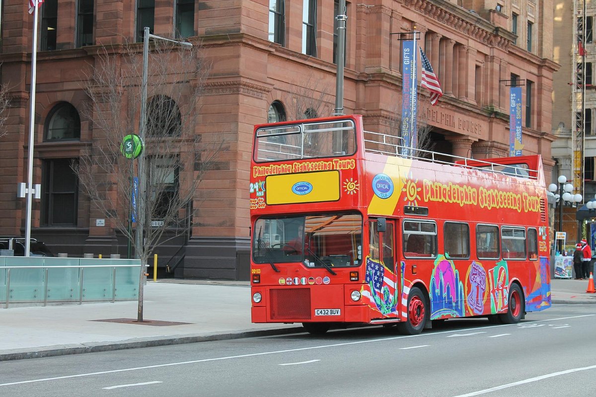 Red open-top tour bus on city street next to a historic building.