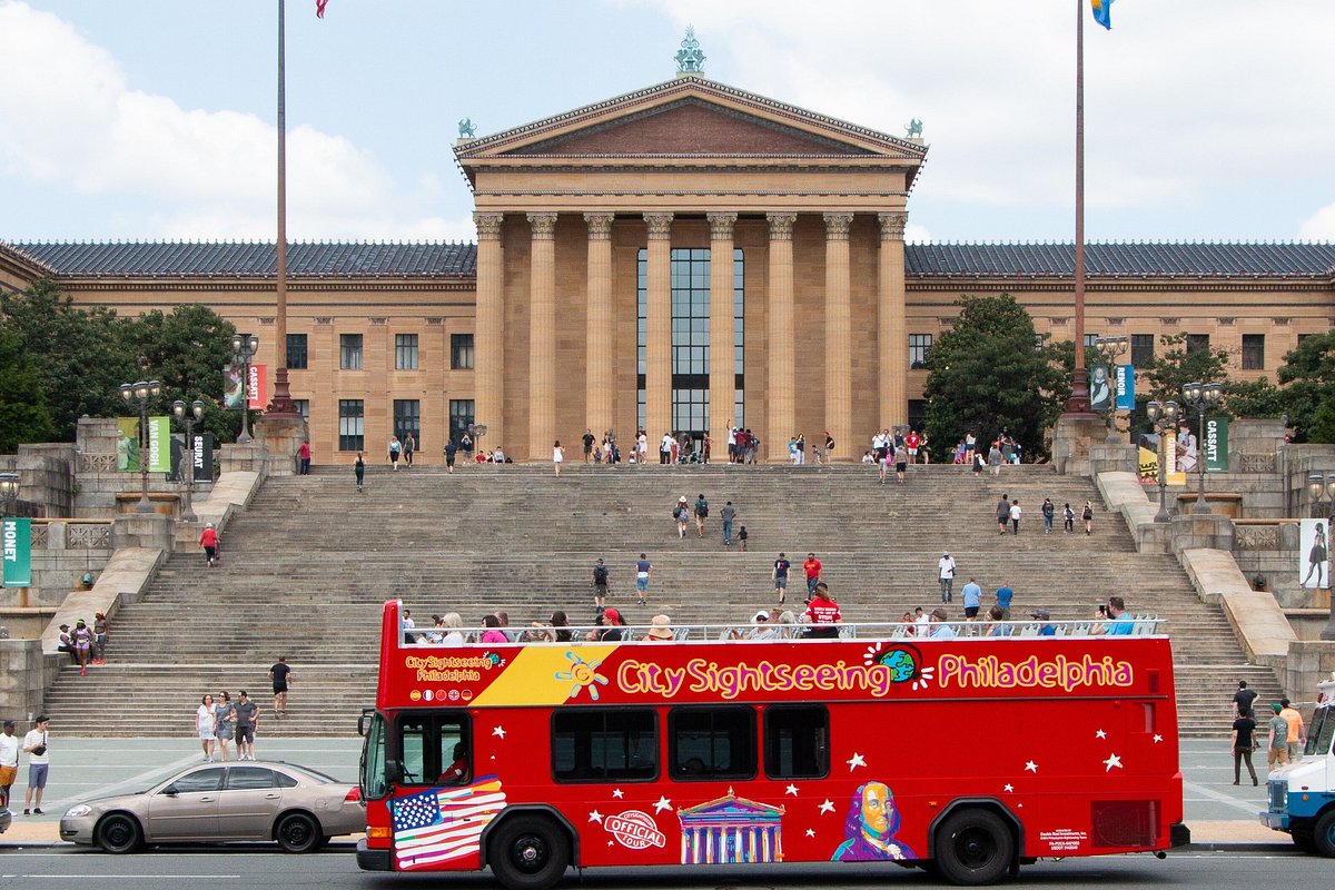 Red sightseeing bus in front of a large museum building with many steps.