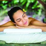 Woman relaxing with eyes closed, lying on a massage table outdoors.