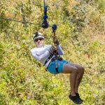 Person zip-lining in outdoor setting wearing helmet and harness.