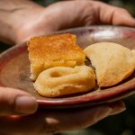 Hands holding a plate with three pastries, including a small pie and a cake slice.