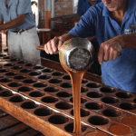Workers pouring caramel into round molds on a wooden table.