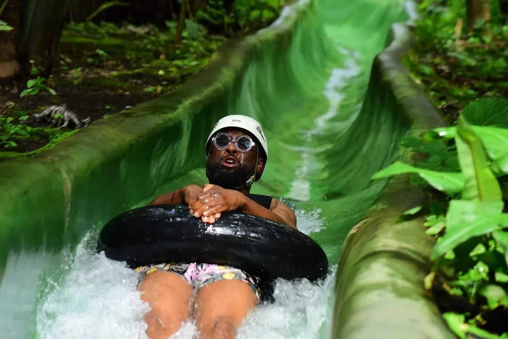 Person riding a water slide on a tube, wearing sunglasses and a helmet.